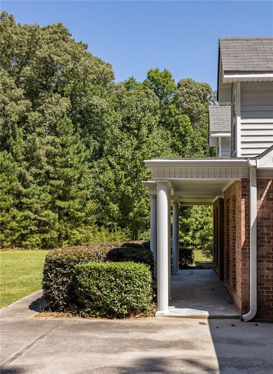 Home’s covered side entrance beside a concrete walkway, trimmed shrubs, and mature trees.