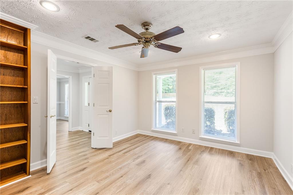 An empty room with light wood floors, built-in shelving, two windows, and a ceiling fan.