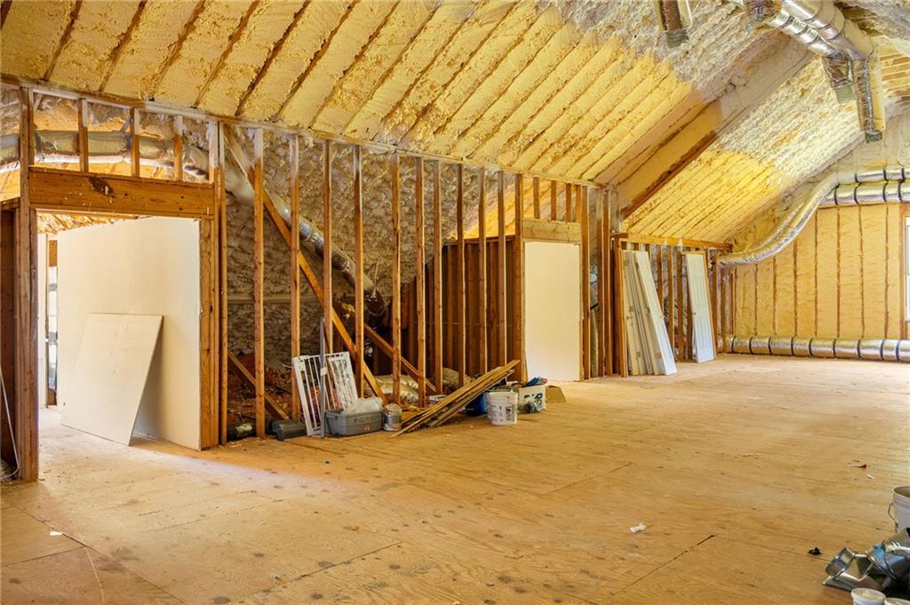 Unfinished room with exposed framing, spray-foam insulation, plywood flooring, and HVAC ducts.