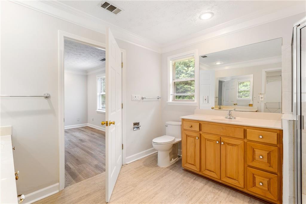 Bathroom with a honey-toned wooden vanity, large mirror, and window beside an open doorway.