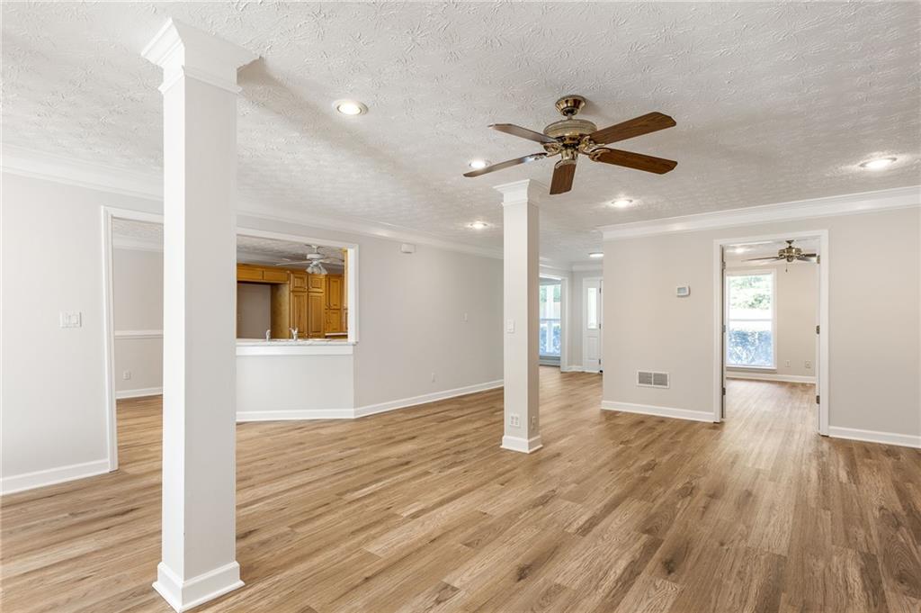 Vacant open living area with wood floors, white columns, and a pass-through to the kitchen.
