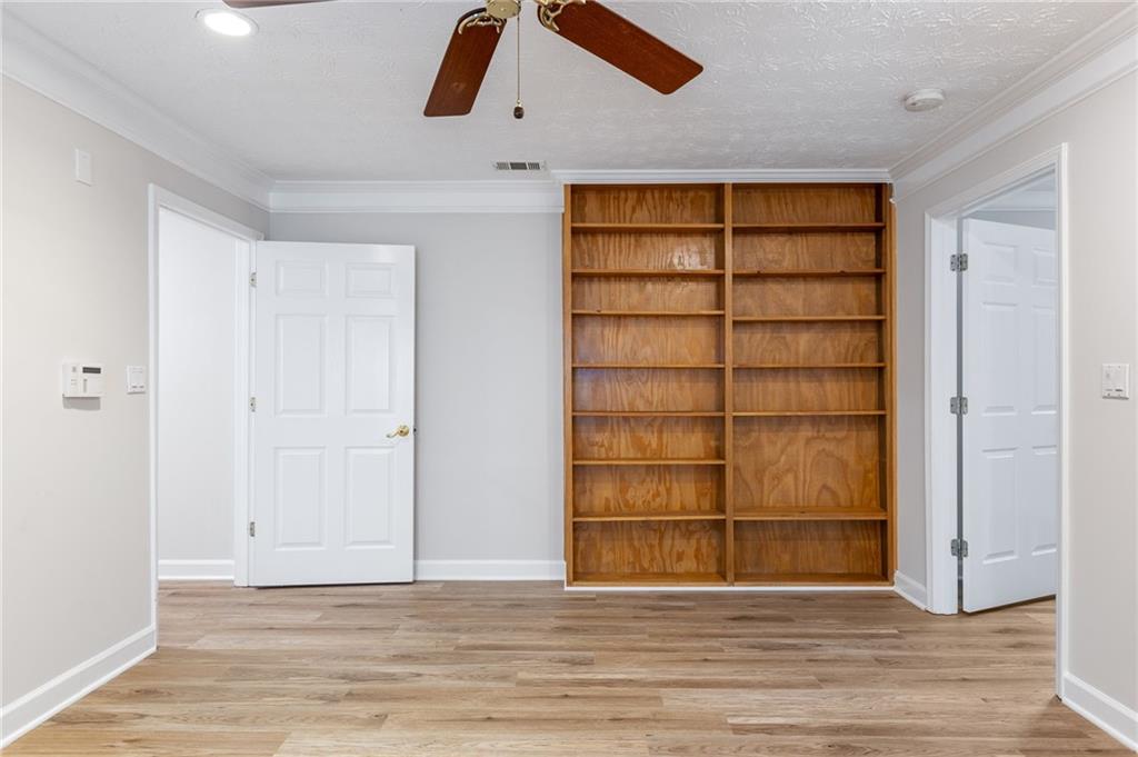 Empty room with a large built-in wooden bookcase and light wood-look flooring.