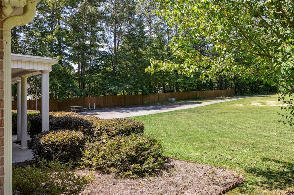 Backyard with a broad lawn, mature trees, wooden fence, paved path, and covered porch.