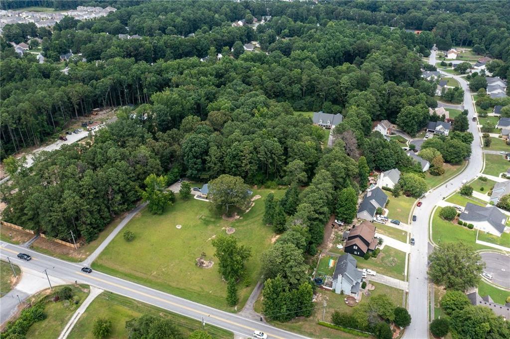 Aerial view of a wooded property with a large grassy clearing beside a road.