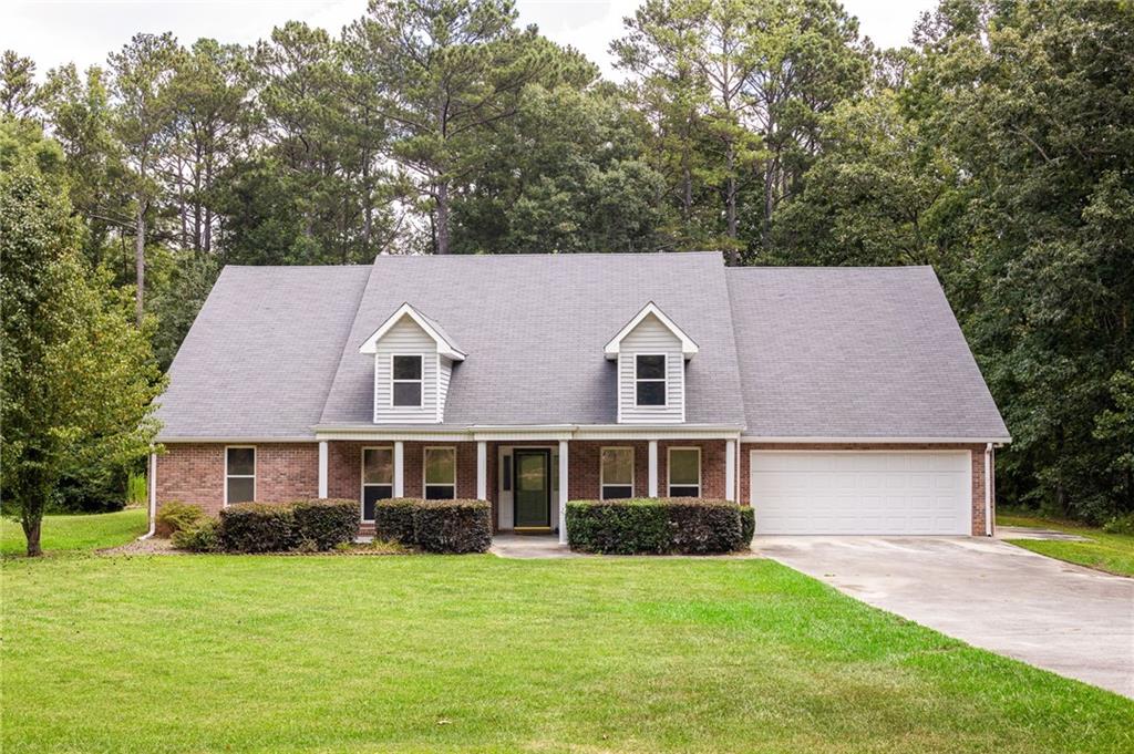Brick house with two roof dormers, an attached garage, and a broad green lawn.