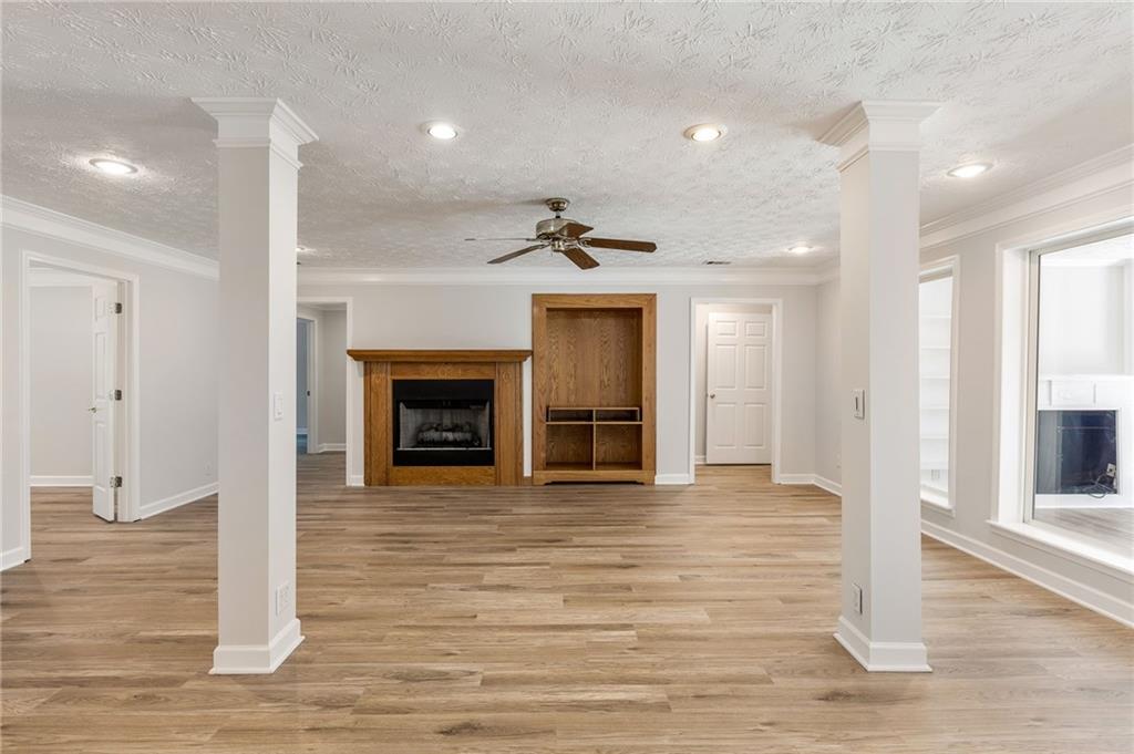 Unfurnished living room with wood-look floors, a fireplace, built-in shelving, and two support columns.
