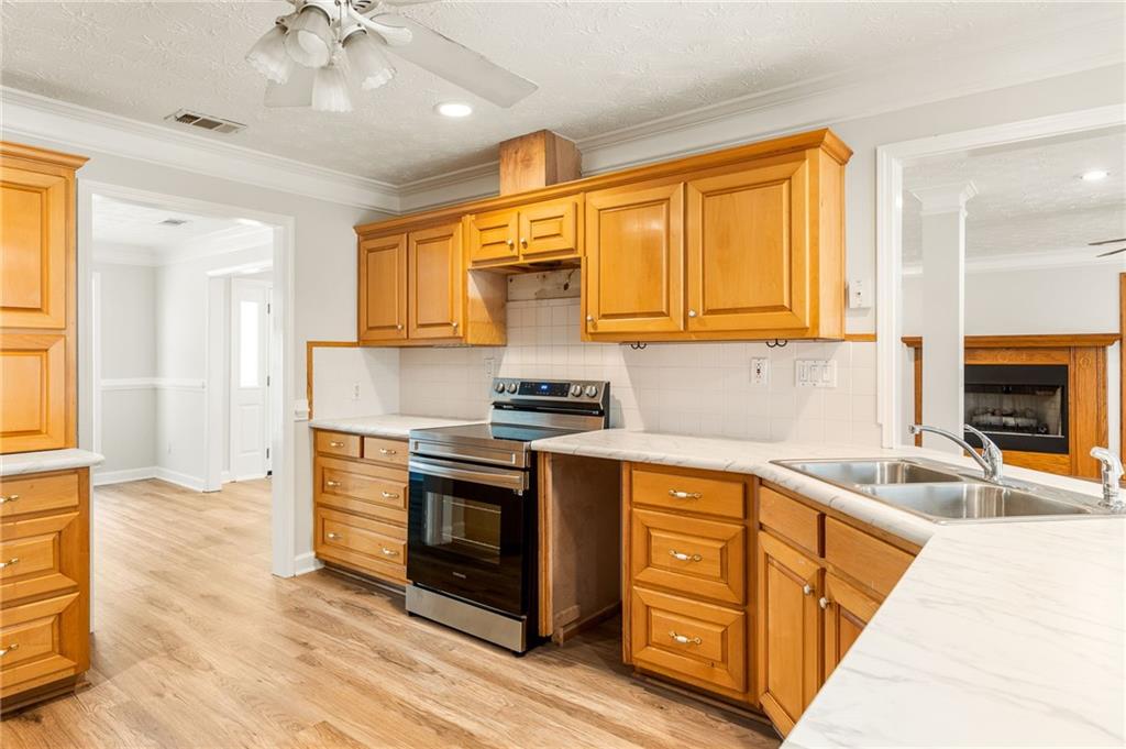 Kitchen with honey-colored cabinets, stainless-steel range, double-basin sink, and light wood-look flooring.
