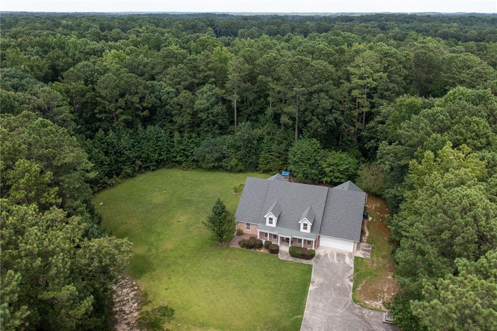 Aerial view of a brick house and driveway bordered by a wide lawn and dense trees.