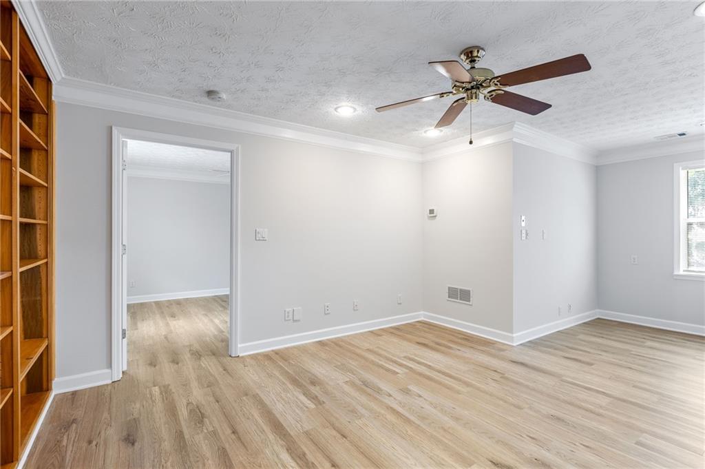 Empty room with light wood flooring, built-in shelves, and a ceiling fan.