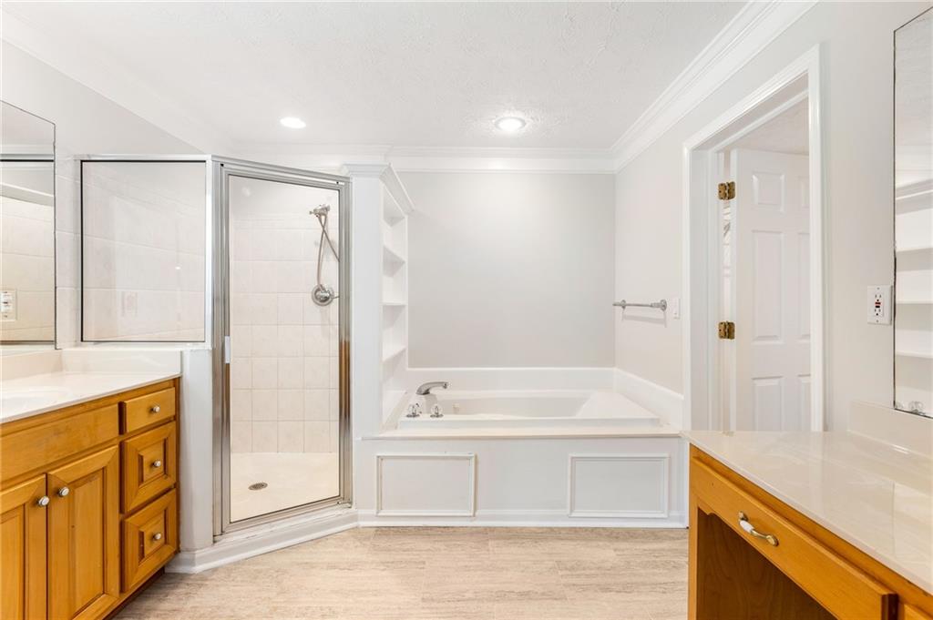 Bathroom with a glass shower, built-in tub, and wood vanities on both sides.