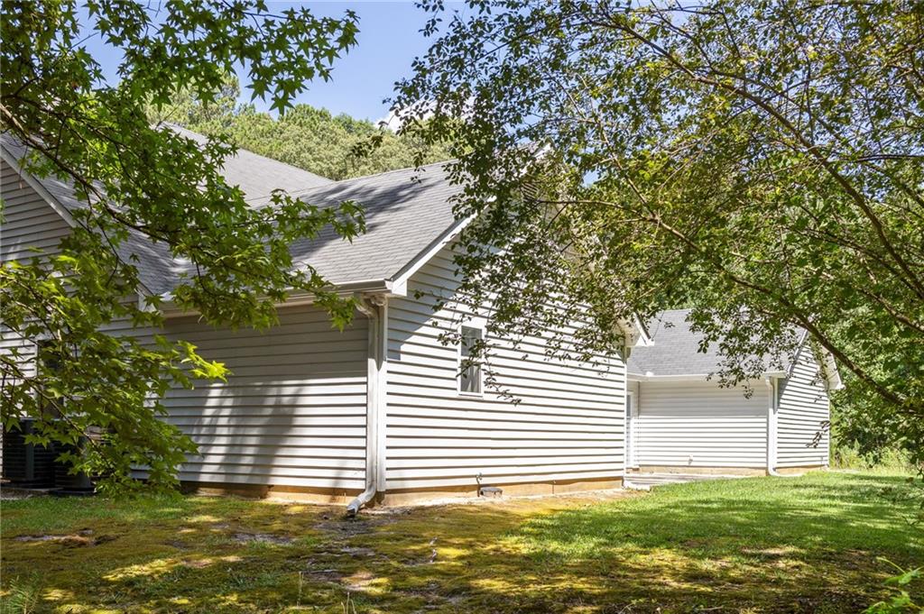 House side exterior with light siding, a gray roof, and leafy trees around the lawn.