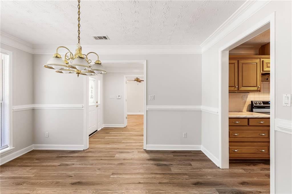 Empty dining room with wood flooring, a brass chandelier, and a view into the kitchen.