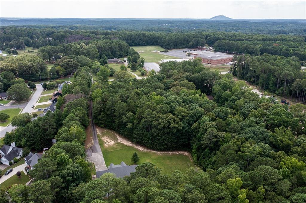 Aerial view of wooded property near homes, with a grassy clearing and a large brick building nearby.