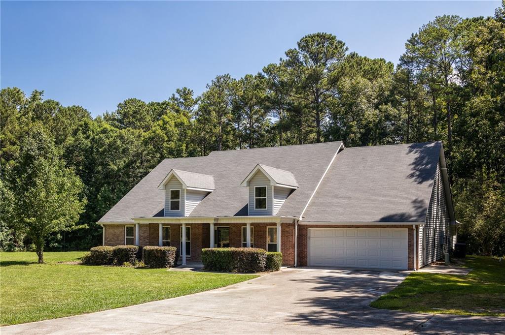 Brick house with two roof dormers, an attached garage, and a wide driveway, backed by mature trees.