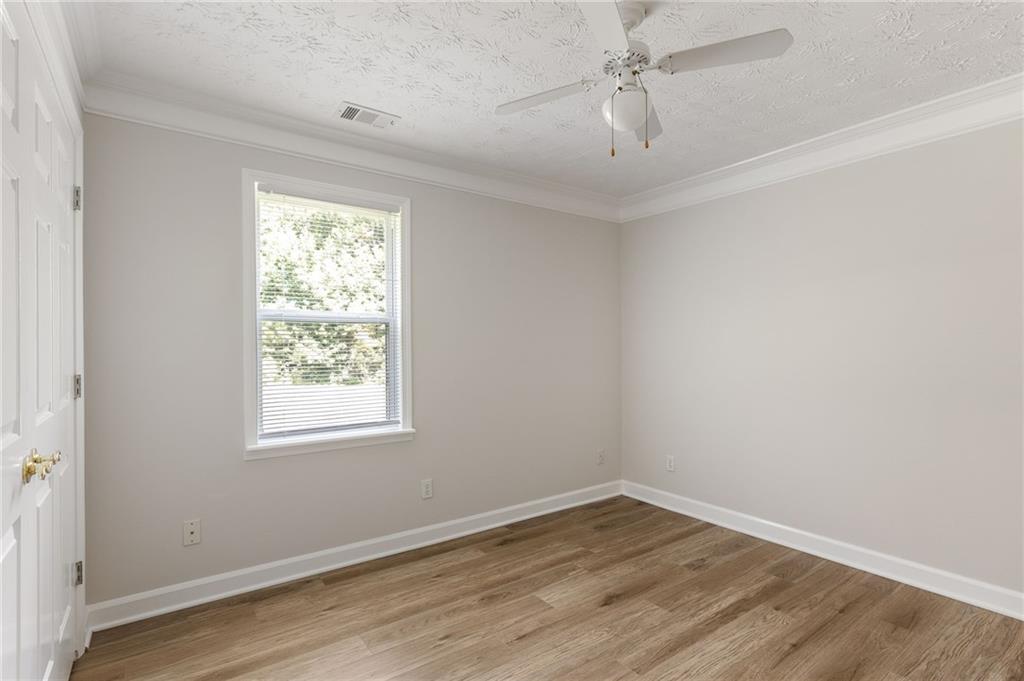 Empty room with wood-look flooring, a window with blinds, and a ceiling fan.