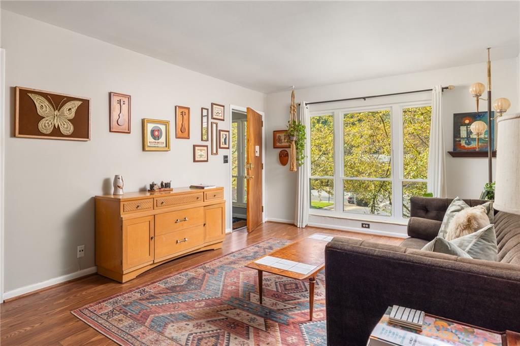 Living room with a patterned rug, wooden sideboard, and large windows overlooking autumn trees.