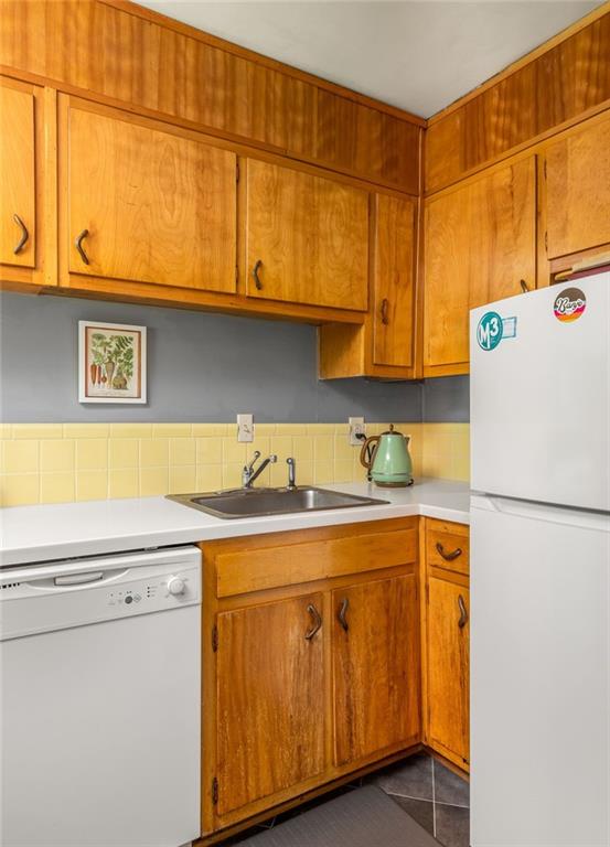 Kitchen with honey-colored wood cabinets, yellow tile backsplash, white appliances, and a green kettle.