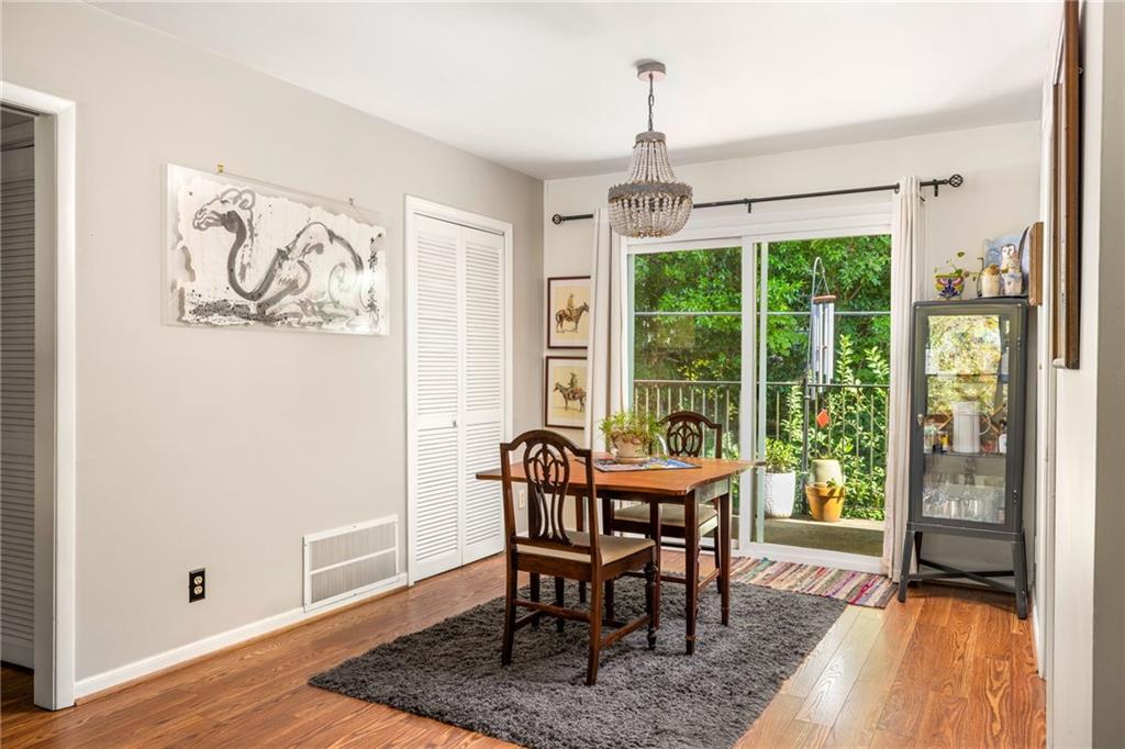 Dining room with a wooden table, chandelier, and sliding doors to a leafy balcony.