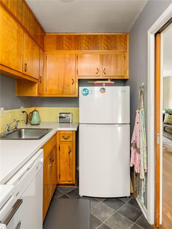 Compact kitchen with honey-colored cabinets, white appliances, and a stainless-steel sink.