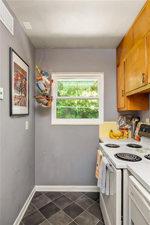 Narrow kitchen with a white electric range, honey-colored cabinets, and a window overlooking greenery.