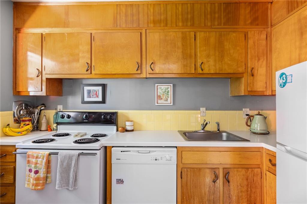 Kitchen with honey-colored wood cabinets, yellow tile backsplash, and white appliances.