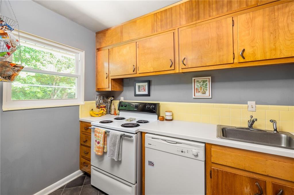 Kitchen with warm wood cabinets, yellow tile backsplash, electric range, and a window overlooking greenery.