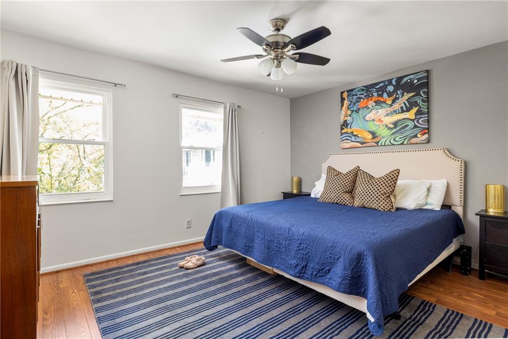 Bedroom with a blue-covered bed, striped rug, hardwood floors, and ceiling fan.