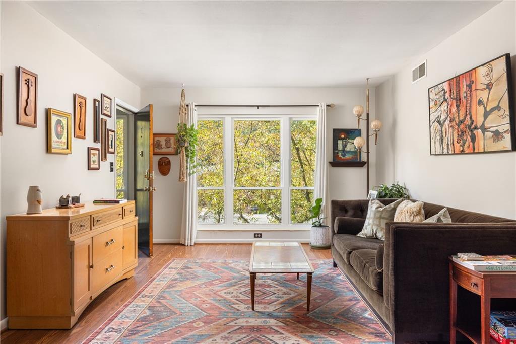 Living room with a brown sofa, patterned rug, and large windows overlooking trees.