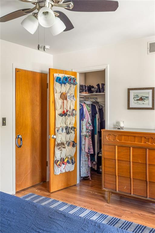 Bedroom with an open closet, hanging clothes, shoe organizer, and wooden dresser.