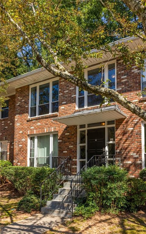 Brick condominium entrance with front steps beneath a large leafy tree.
