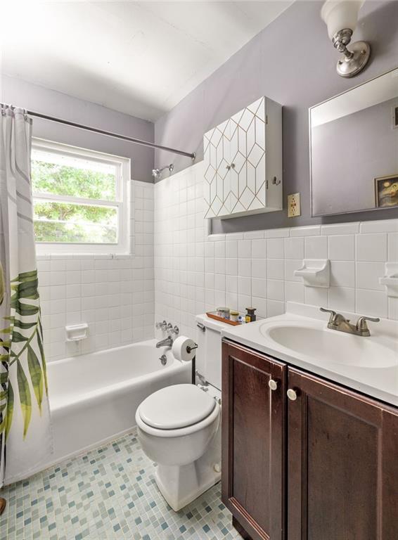 Bathroom with a white tub, tiled walls, patterned floor, dark wood vanity, and window.