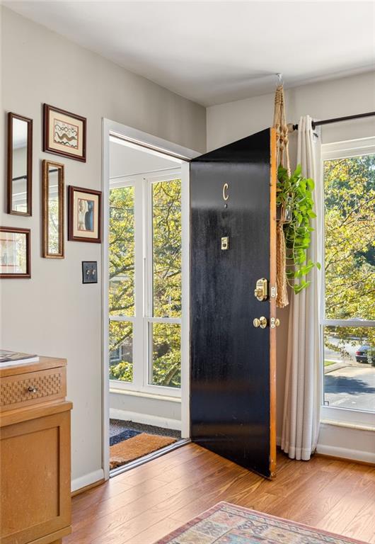 Entryway with an open black front door, framed pictures, and windows overlooking autumn foliage.