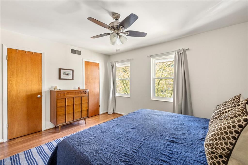 Bedroom with a blue quilted bed, hardwood floors, and two curtained windows.