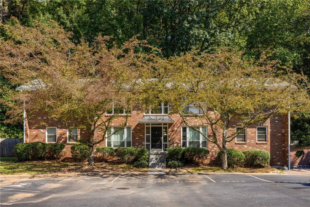 Red-brick residential building with a central entrance, mature trees, and parking spaces in front.
