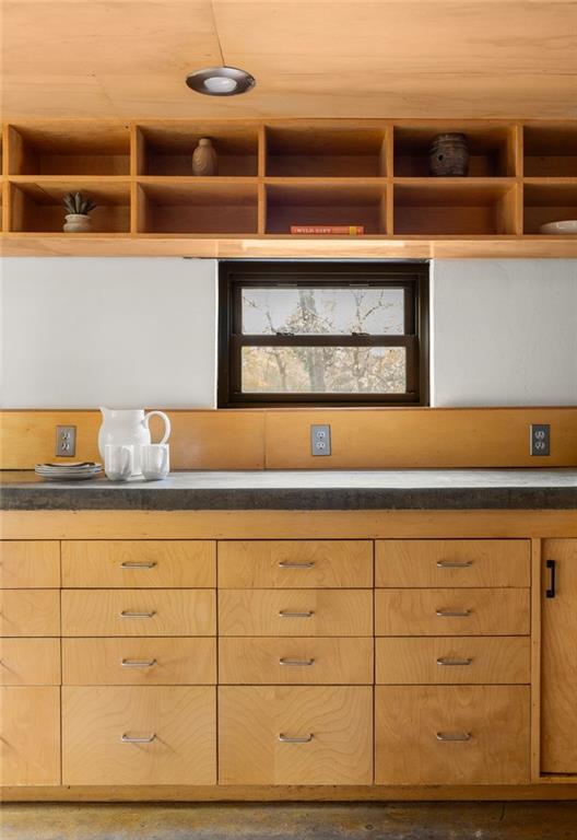 Kitchen with honey-colored wood cabinetry, open shelving, and a small centered window.