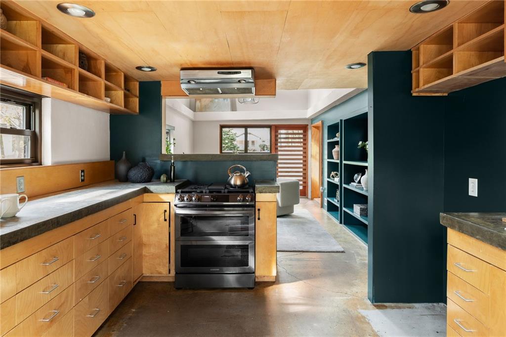 Kitchen with teal walls, warm wood cabinetry, open shelving, and a stainless steel range.