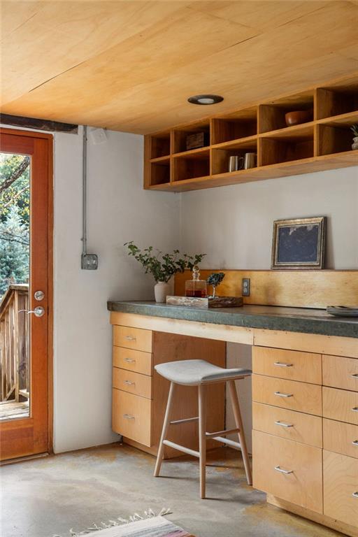 Built-in workspace with light wood cabinets, open shelves, and a stool beside a glass-paneled door.