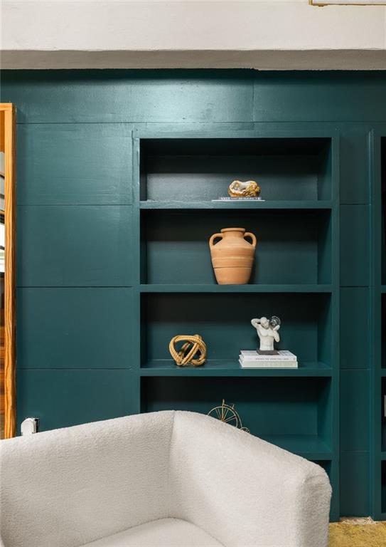 Dark teal built-in shelves with pottery behind a cream upholstered chair.