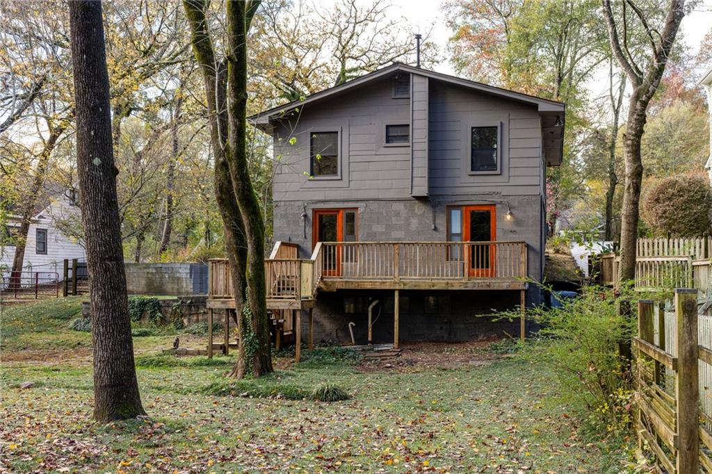 Rear exterior of a gray two-story home with a raised wooden deck in a wooded yard.