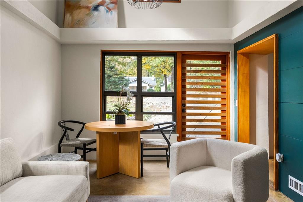 Living and dining area with a round wood table, large windows, and a teal accent wall.