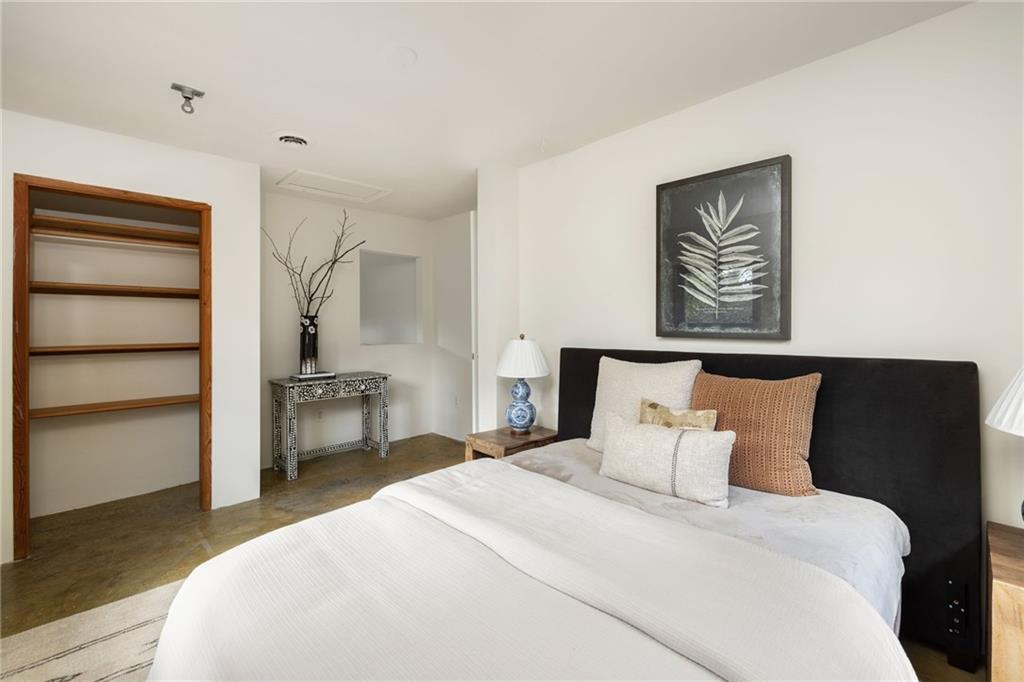 Staged bedroom with a white bed, dark headboard, built-in wooden shelves, and botanical wall art.