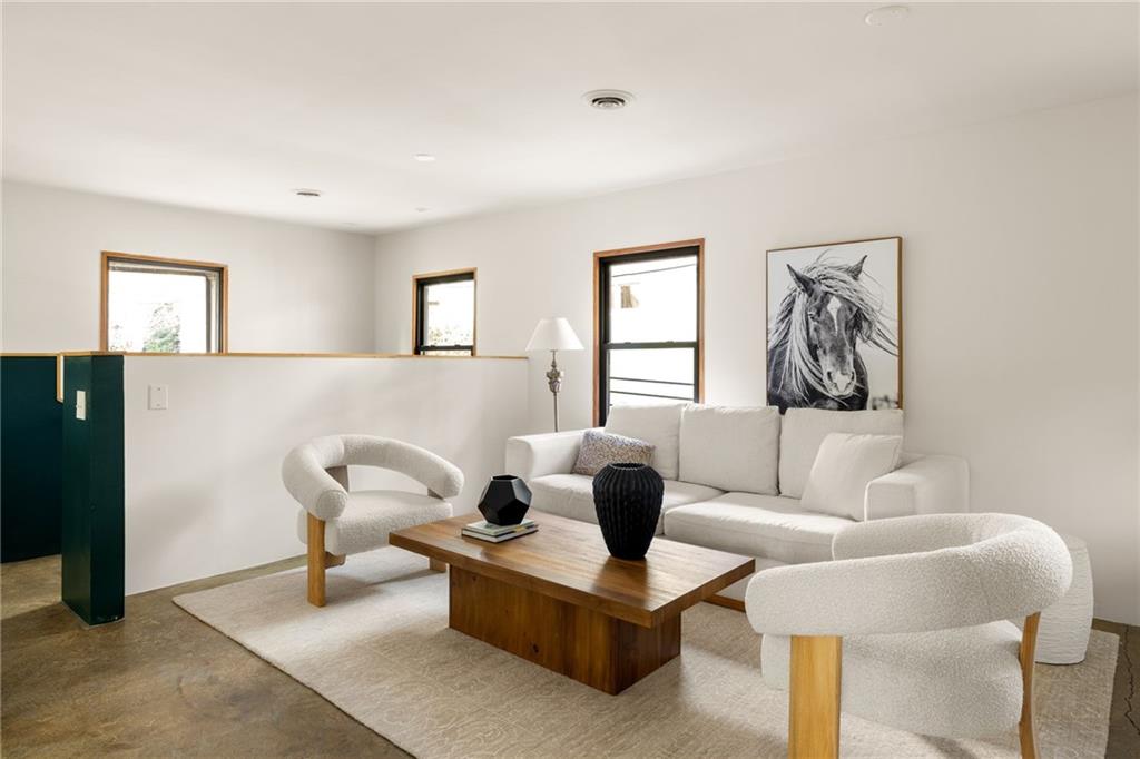 Staged living room with white seating, a wooden coffee table, concrete floors, and a horse portrait.