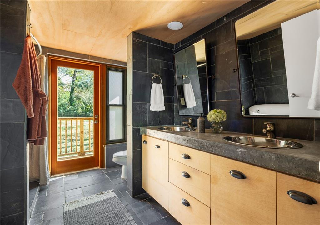 Bathroom with a double vanity, dark slate tile, and a wood-framed door to a balcony.