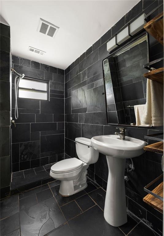 Bathroom with charcoal tile, a white pedestal sink and toilet, and a small frosted window.
