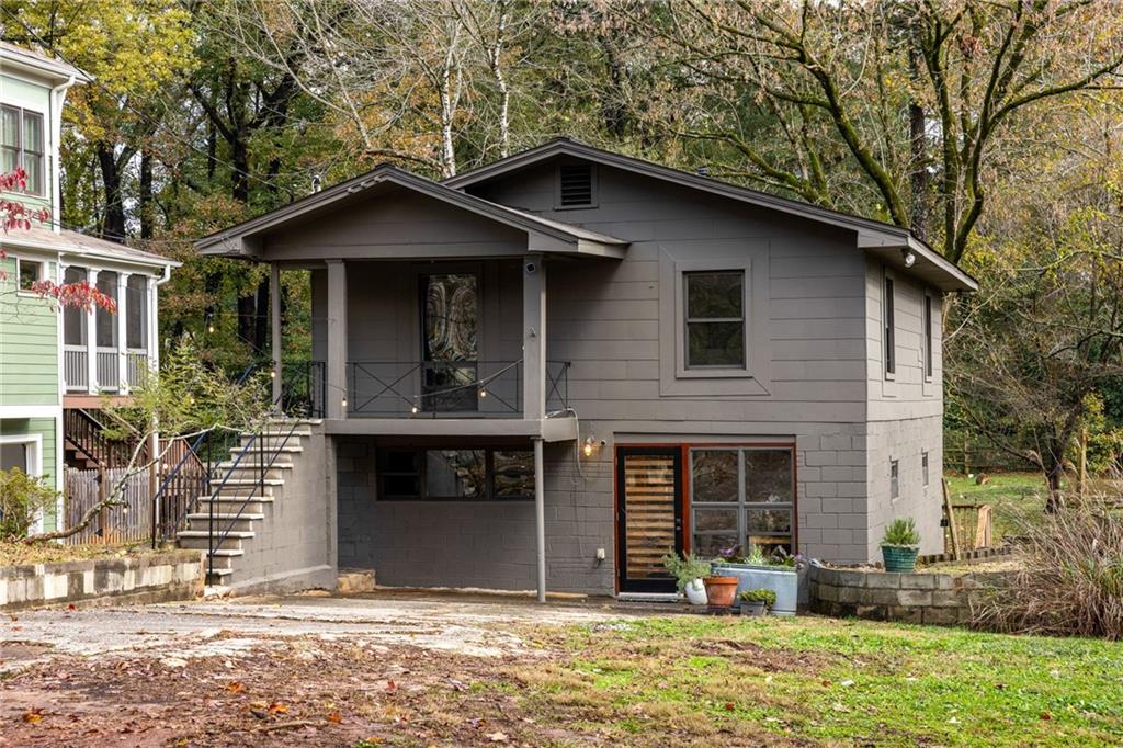 Gray split-level home with a covered upper porch and exterior stairs beneath mature trees.