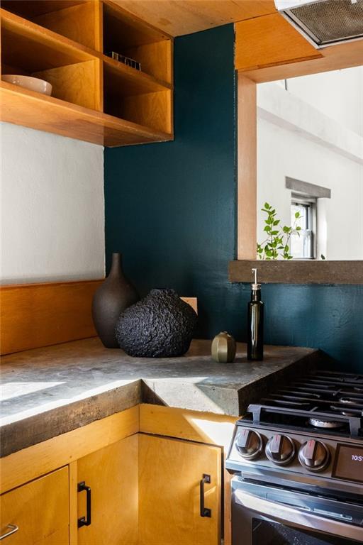 Kitchen with warm wood cabinets, concrete counters, and a dark teal accent wall.
