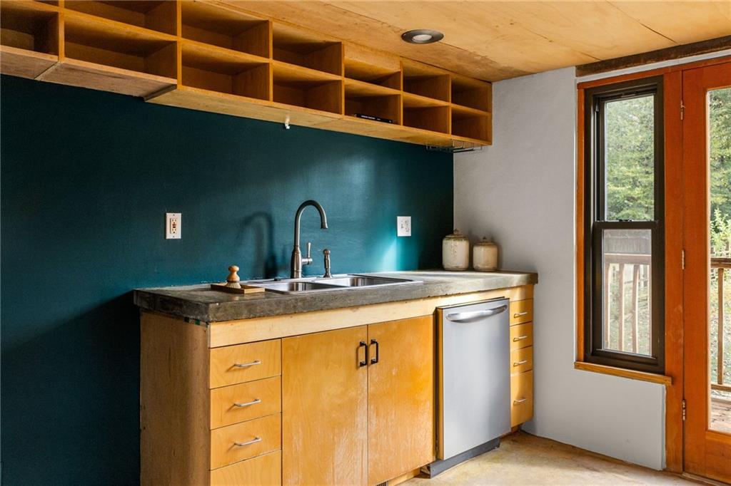 Kitchen with teal wall, open wood shelving, double sink, and a glazed door to the deck.