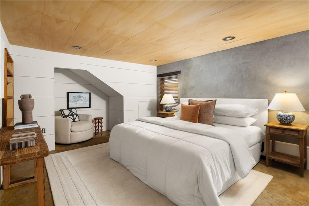 Bedroom with a white bed, wood ceiling, gray accent wall, and tucked-away sitting nook.