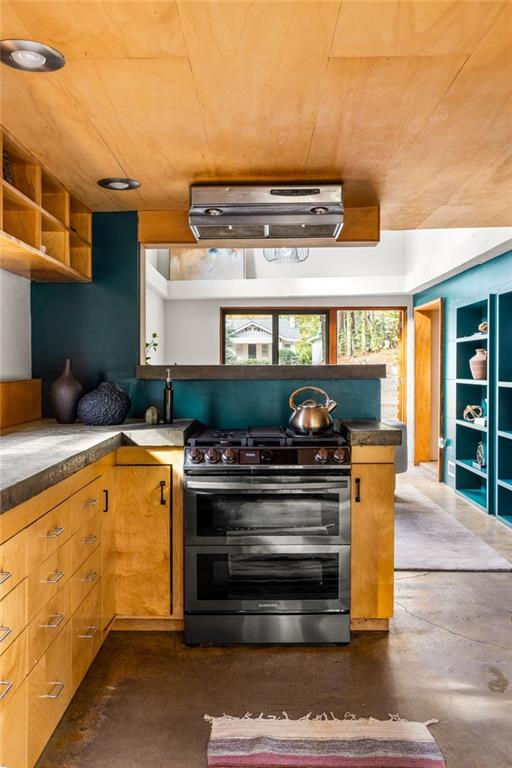 Kitchen with teal walls, wood cabinetry and ceiling, and a stainless steel range beneath a window.