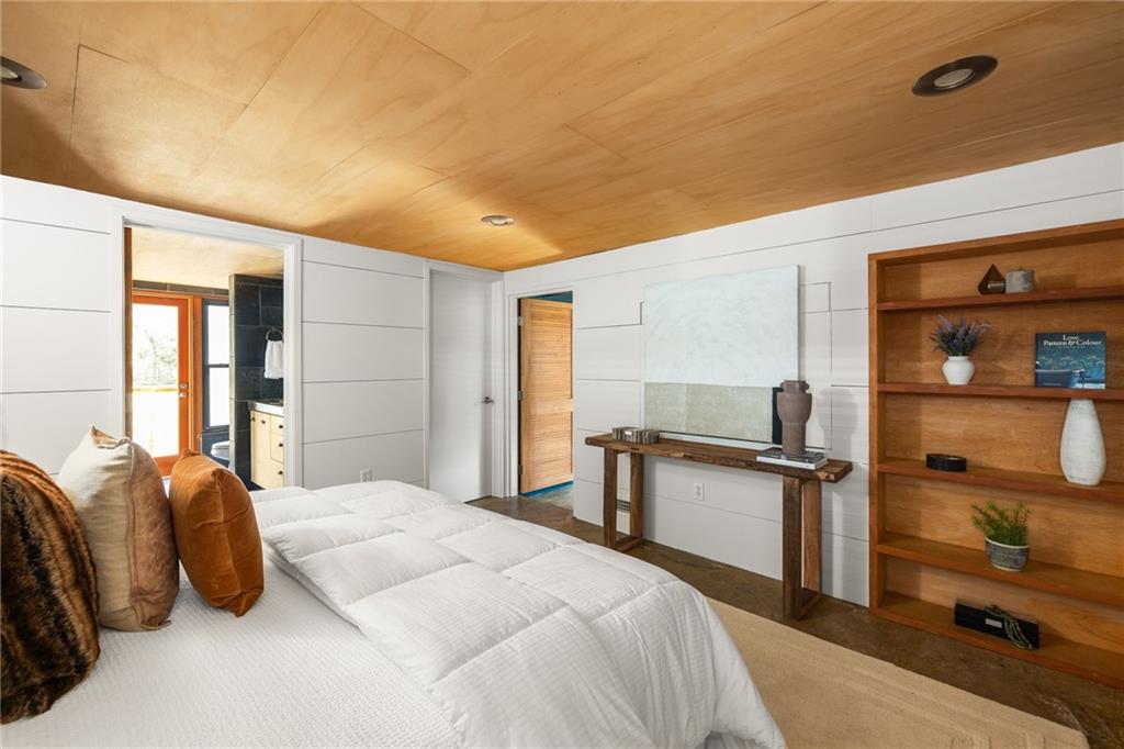 Bedroom with a white quilted bed, wood ceiling, and built-in shelving.